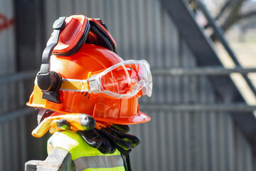 Naklejka na ściany i meble Construction safety helmet with protective goggles, ear protection and work gloves at building site. Personal protective equipment for industrial work, construction safety and workplace protection.