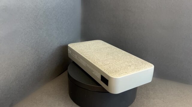 Power bank gris claro con textura de tela girando en estudio