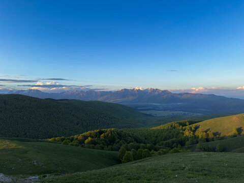 Panorama montano con valli verdi sotto cielo azzurro cristallino.