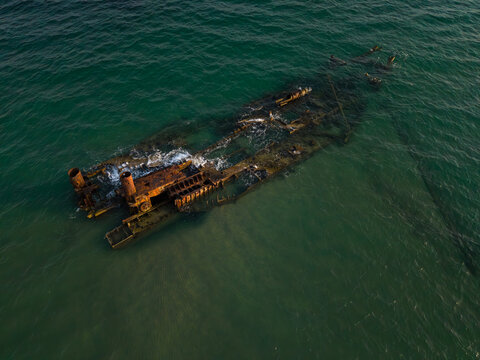Aerial view of a sunken shipwreck near Epanomi beach, Thessaloniki, Greece. Old rusty vessel in turquoise Mediterranean water surrounded by sand and sea textures, dramatic coastal landscape.
