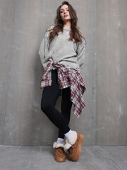 Fototapeta premium Stylish Young Woman in Cozy Sweater and Leggings Paired with Comfortable Footwear Against a Textured Background
