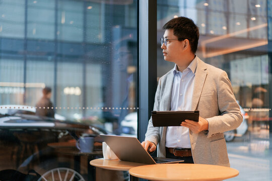 Businessman holding tablet and gazing out of window in modern office setting
