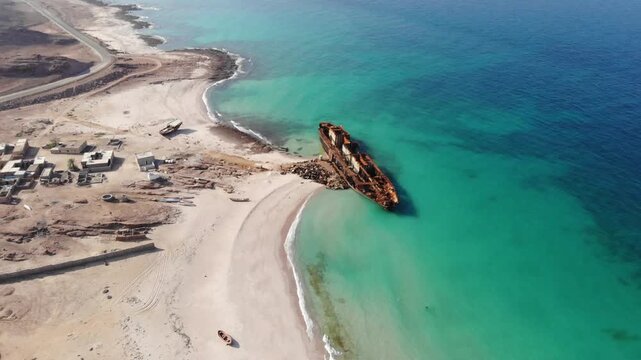 Panoramic aerial video of Socotra Island's coastline featuring an abandoned shipwreck on a turquoise beach, ideal for travel, historical, and adventure themes