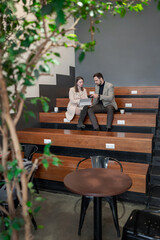 Fototapeta premium Business partners discussing ideas and reviewing tasks on wooden seating beneath green leaves. Ideas, tasks, green leaves, discussion, business.