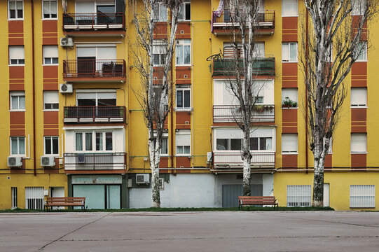 Colorful residential apartment building facade with balconies, trees and empty benches in a public square in M&oacute;stoles, Madrid, Spain. Urban housing architecture representing everyday life in Spain.