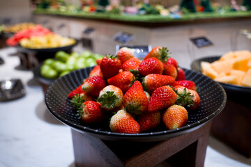Fresh strawberries in a black bowl on a buffet fruit station