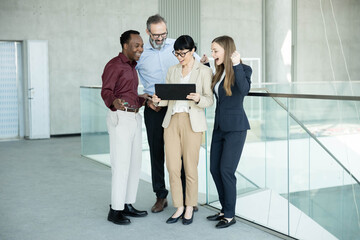 Fototapeta premium Business people of various ages and ethnicities joyfully celebrating their success while looking at a digital tablet at the office