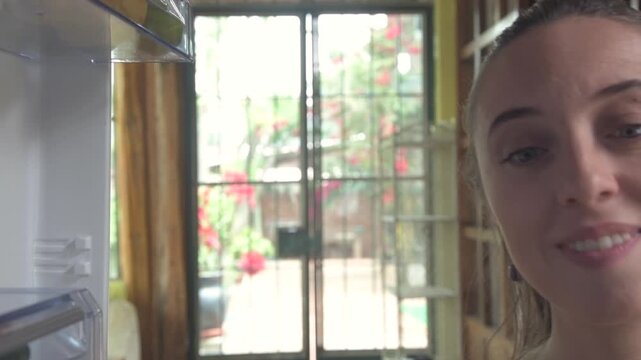 Point of view shot from inside a refrigerator as a young woman opens the fridge and looks inside at fresh fruit. Concept of healthy eating, home lifestyle, and choosing nutritious food in a modern kit