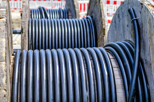Construction work takes place near a road with bright green cable on a large spool during daytime in a city area
