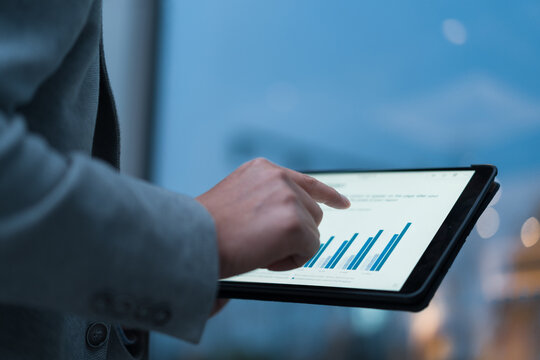 Business professional holding tablet and analyzing data charts with finger touch