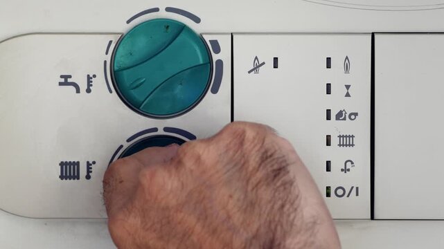 Hand adjusting temperature knobs and pressing reset button on domestic water heater control panel. Man setting home heating system for energy efficiency and hot water supply.