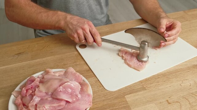 Person using meat tenderizer on raw chicken. Chef preparing pork loin slice with meat mallet on cutting board. Man tenderizing fillet. Cooking cutlets pounding poultry breast close-up. Culinary dish.