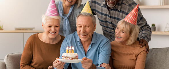 Fototapeta premium Friends gather in a cozy living room to celebrate a birthday. One person holds a cake with candles. Everyone smiles and enjoys the moment together.
