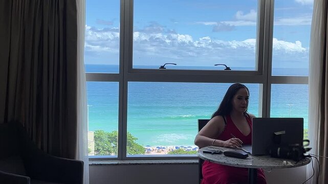 Freelancer woman working online while enjoying ocean view vacation setting in Brazil, in Brazil Rio de Janeiro look down camera medium shot