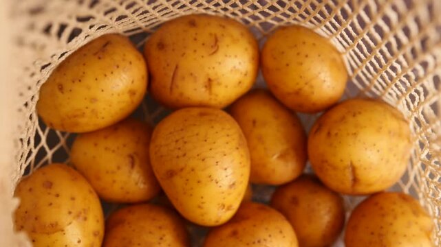 Many newly purchased yellow potatoes fill a woven cream string bag resting on a light grey counter, ready for cooking.