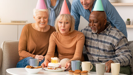 Fototapeta premium A group of friends gathers in a living room to celebrate a birthday. They are smiling and enjoying cake with candles. The atmosphere is joyful and filled with friendship.