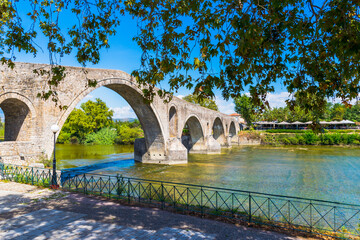 Obraz premium Famous medieval arched Arta's Bridge in Arta town with walkway and trees in Epirus region, Greece