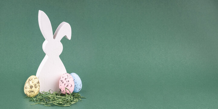 Wei&szlig;er Osterhase aus Holz mit bunten Ostereiern auf gr&uuml;nem Hintergrund mit Textfreiraum