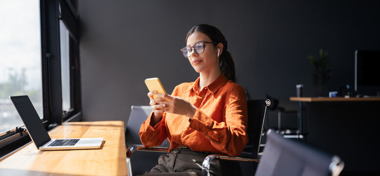 Young Indian business woman manager ceo using cell phone mobile app laptop. Latin Hispanic mature female businesswoman holding smartphone in office trading, working online. Web banner, copy space