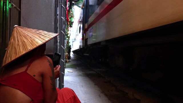 Tourist wearing a conical hat watching a passing train on Hanoi Train Street