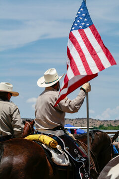 Cowboys carrying an American flag on horseback at a small town rodeo