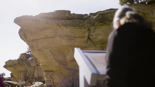 Person Reading Information Sign at Native American Rock Art Site with Cliffs Behind