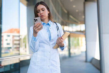 Fototapeta premium Medical professional viewing smartphone outside clinic building