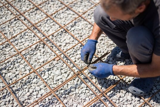 Construction worker tying steel rebar mesh on site