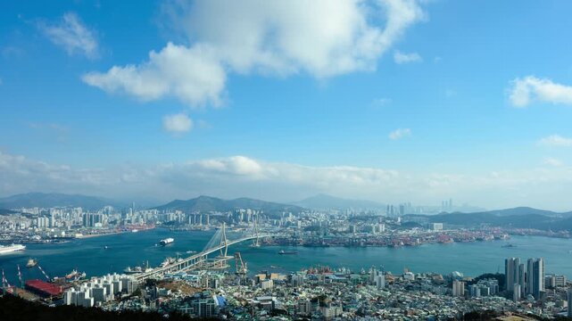Timelapse of Busan Harbor Bridge and busy Busan port with ship traffic and moving clouds, wide angle view from Bongrae Mountain