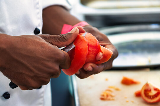 African Chef Peeling a Fresh Tomato with a Paring Knife in a Professional Kitchen