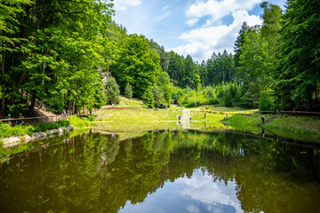 Obraz premium Visitors enjoy the Pelisek water reservoir located near Prachovske sandstone rocks in Czechia. This spot features green trees, clear water, and rocky landscapes.