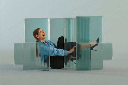 Laughing business woman sitting among translucent glass blocks 3D structure in studio