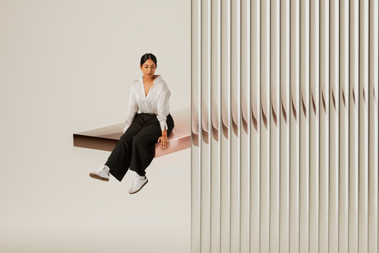 Latin woman sitting on floating copper 3D platform beside ribbed architectural wall