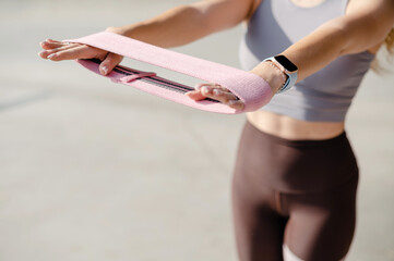 Woman's hands holding a pink resistance band for glute workout outdoors