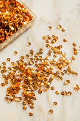 scattered pile of golden metallic sequins on white marble