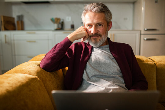 Senior man relaxing with laptop on sofa in home kitchen