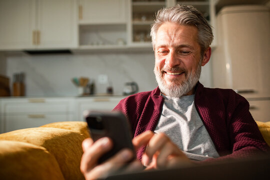 Smiling senior man using smartphone on sofa at home