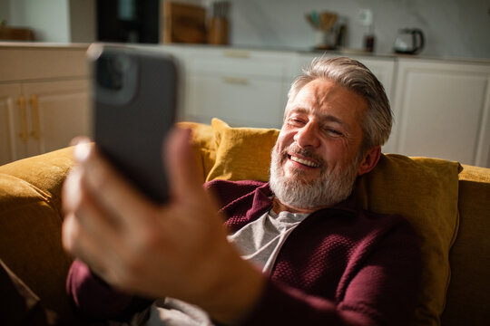 Smiling middle-aged man using smartphone on sofa at home