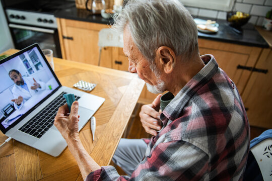Senior man consulting online doctor at home about inhaler