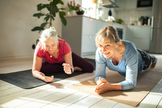 Two senior women doing plank exercise in a home kitchen