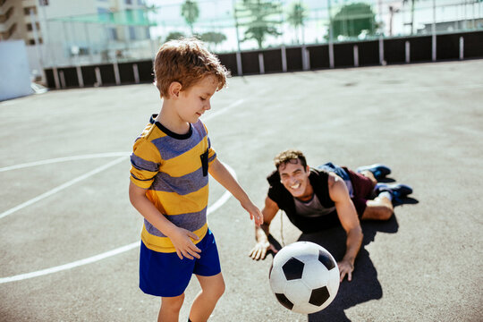 Boy playing soccer with adult on sunny outdoor court