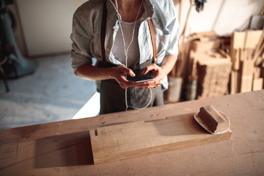 Woodworker using smartphone and headphones in workshop