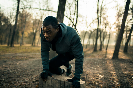 Young man doing outdoor workout on tree stump in forest park