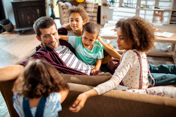 Obraz premium Father bonding with four children on living room sofa at home