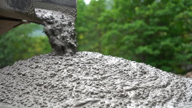 Cement pours from a mixer onto a large pile of aggregate outdoors