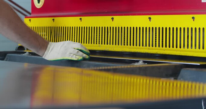Metal sheet fed into industrial guillotine cutting machine during operation. Factory workflow and blue collar labor in metalworking production