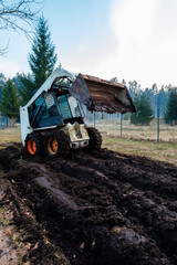 Fototapeta premium Skid Steer Loader on Muddy Track with Raised Bucket and Wire Fence