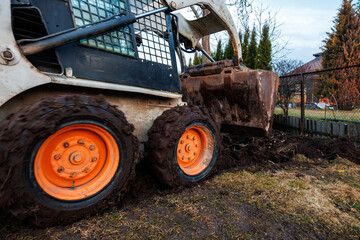 Skid steer loader digs wet soil along residential fence line