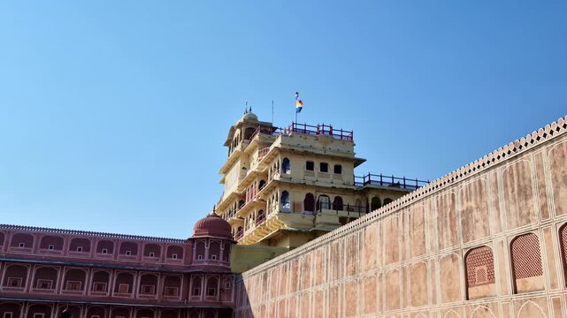 The Chandra Mahal rises above the fortified walls of Jaipur�s City Palace under a clear blue sky. A colorful flag flies atop the multi-storied cream and pink Rajput structure.
