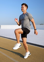 Obraz premium Energetic man training with high knees on an outdoor athletic track under a bright clear blue sky in daytime